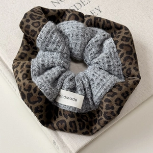 Close-up of leopard print fabric and grey knit texture with a Handmade label on scrunchie