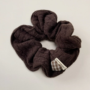 Detailed close-up of dark brown knit scrunchie featuring checkered heart patch and woven label
