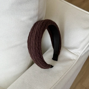 Détail d'un serre-tête épais en tricot marron foncé montrant le motif de torsades