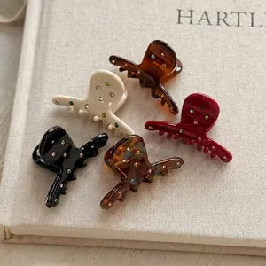Five colorful acetate hair claws with rhinestones on a warm textured book background