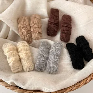 Five pairs of knitted wool hair clips in soft autumn colors displayed in a woven basket