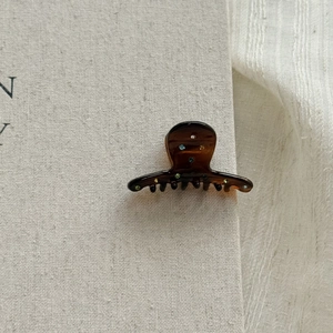 Detail of mini tortoiseshell hair claw with colorful rhinestones on a beige book