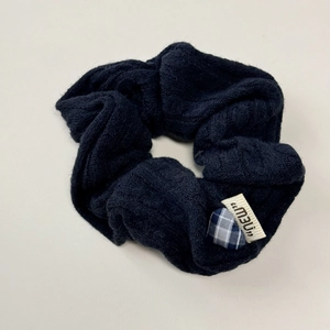 Detail of navy blue knitted scrunchie featuring a checkered heart charm and new tag