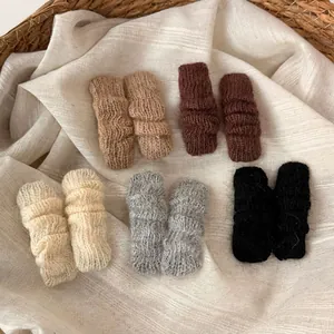 Knitted wavy hair clips in five neutral colors displayed in a woven basket