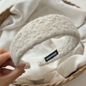 Detailed close-up of cream-white curly wool headband showing the handmade label and texture