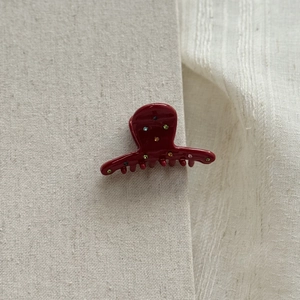 Detail of red acetate hair claw with sparkling colored rhinestones on grey fabric