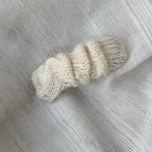 Detailed view of hand-knitted wave hair clip in creamy white yarn on fabric