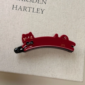 Detailed view of dark red acetate cat hair clip with handmade gold lettering