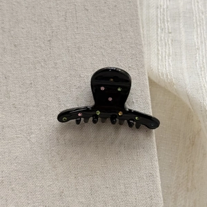 Close-up of black acetate hair claw with multicolored rhinestones on textured fabric