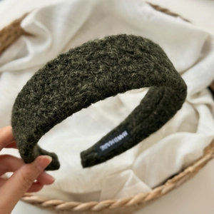 Detail of dark green fuzzy curly texture headband with a handmade label on white fabric