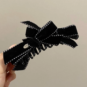 Detail view of black velvet bow hair clip with white polka dot stitching and silver brand logo