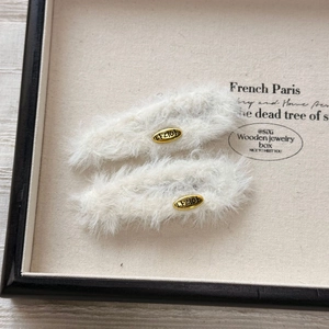 Macro view of white faux fur headbands featuring golden oval metal plates with engraving