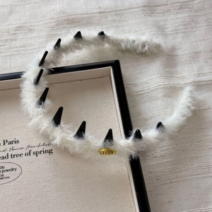 Detail of white faux fur headband with black spikes and gold metal logo plaque