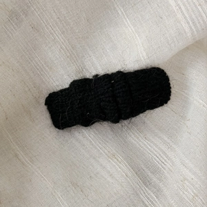 Close-up of black knitted hair clip with soft mohair texture on a beige linen fabric
