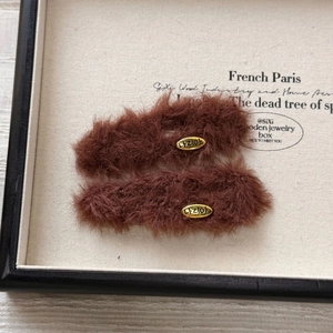 Close-up of brown plush hair clips with gold metal oval label and soft fur texture