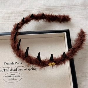 Detail view of brown plush headband with black anti-slip teeth and a gold metal label