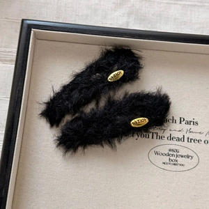 Detail of black plush hair clips featuring golden oval metal buckles on a cream background