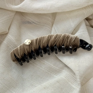 Close-up of handmade golden charm on velvet wrapped banana hair clip on linen background