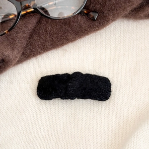 Détail d'une pince à cheveux rectangulaire en tricot noir avec bords ondulés doux