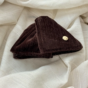 Close-up of deep brown velvet hair clip with a round golden metal logo plaque