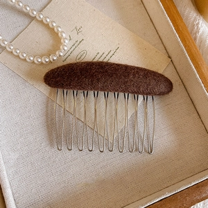 Detail of wool felt vintage hair comb with ten silver metal teeth on a wooden tray