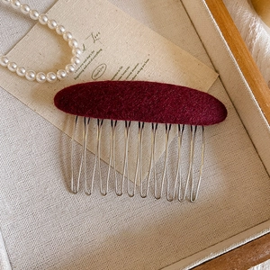 Detail of burgundy felt hair comb with 10 silver metal teeth on a vintage wooden tray