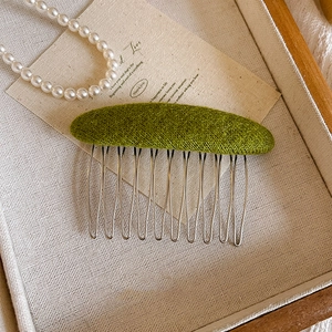 Detailed view of a vintage green wool felt hair comb with ten silver metal wire teeth
