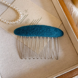 Detailed close-up of dark green wool felt hair comb with ten silver metal teeth