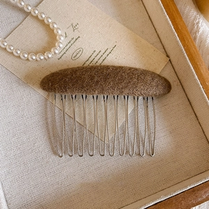 Detail of a brown wool felt hair comb with ten silver metal teeth on a wooden tray