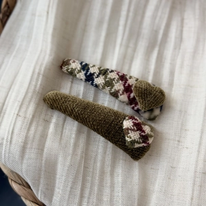 Detail view of retro green tweed bow hair clips set on textured white fabric background