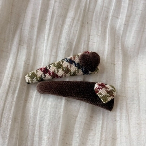 Detail view of retro plaid hair clips with plush hearts on white fabric background
