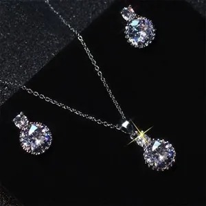 Macro shot of silver zircon feather pendant and earrings on black velvet display