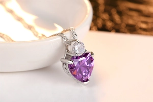 Macro shot of silver heart necklace with purple zircon and sparkling bokeh background
