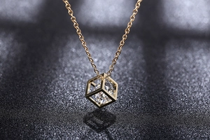 Close-up of a gold hollow cube pendant necklace featuring a brilliant faceted zircon