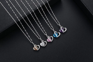 Detail view of five double-heart necklaces with colorful crystals on black texture