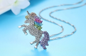 Détail d'un collier licorne en argent serti de strass colorés sur un fond bleu clair