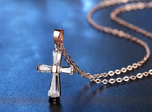 Détail du collier croix en or rose avec cristaux de zircon taille baguette sur fond foncé