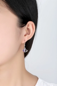 Close-up of a model wearing heart-shaped silver earrings with purple zircon crystals
