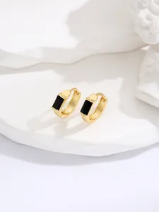 Detailed macro view of gold huggie earrings featuring a minimalist square black gemstone