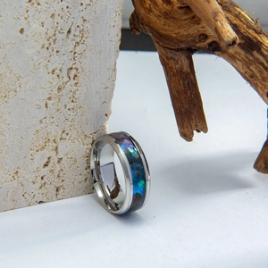 Polished titanium steel men's ring with colorful abalone shell inlay on stone and wood base