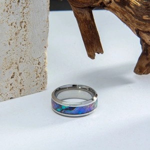 Macro shot of men's titanium steel ring featuring colorful abalone shell inlay on wood