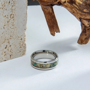 Macro detail of men's wide titanium ring with natural shell inlay on a stone background