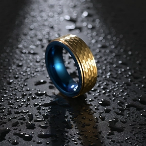 Bague en tungstène martelé doré avec intérieur bleu et gouttes d'eau sur fond noir mat