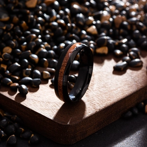 Macro detail of men's black titanium ring with red wood inlay on dark pebbles