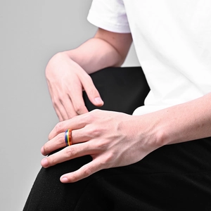 Close-up of a rainbow enamel pride ring worn on a finger against a clean grey backdrop