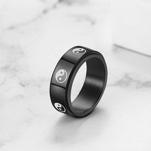 Macro view of black stainless steel spinner ring with white Tai Chi symbols on marble surface