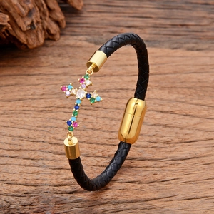 Detail of black braided leather bracelet with golden cross pendant and colorful zircons