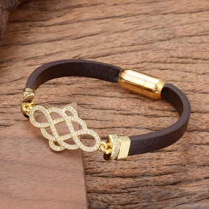 Brown braided leather bracelet with golden zircon knot and magnetic clasp on wood