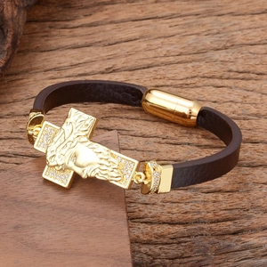 Détail d'un bracelet en cuir marron tressé avec pendentif croix de Jésus dorée et fermoir aimant