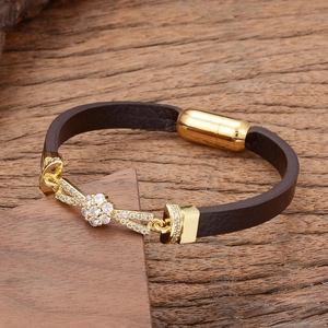Detail of dark brown leather bracelet with sparkling gold flower charm on wood